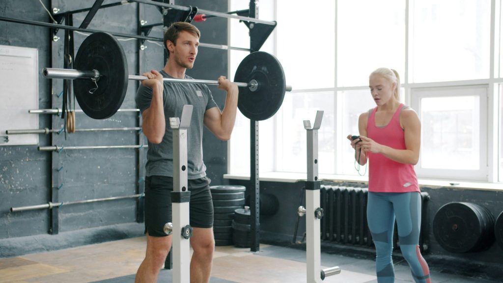 Man lifting weights with woman watching