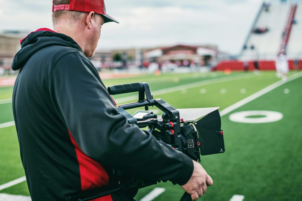 man in black and red long sleeve shirt holding black video camera during daytime